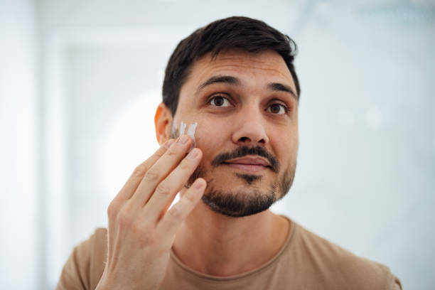 istock Handsome Man Applying Face Cream on his Cheek in the Bathroom 1390155854
