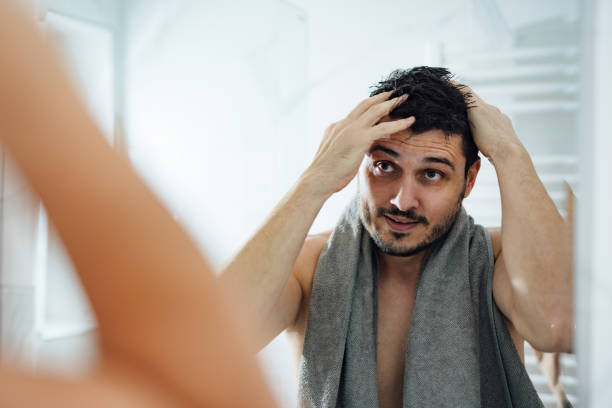 Handsome Man Styling his Hair in a Bathroom Happy man touching his wet hair while looking into the mirror in the morning. body care shower stock pictures, royalty-free photos & images