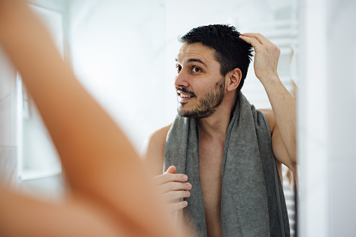 Happy man touching his wet hair while looking into the mirror in the morning.