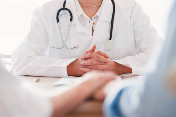 Mature couple holding hands at a doctors office. Mature couple holding hands at a doctors office. Doctor can be seen in the background. infertility stock pictures, royalty-free photos & images