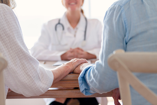 Mature couple holding hands at a doctors office. Doctor can be seen smiling in the background.