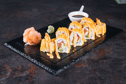 Set of sushi rolls with cream cheese, rice and salmon on a black board decorated with soy sauce and avocado on a dark wooden background. Japanese cuisine. Food photo background