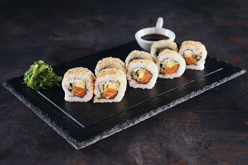 Set of sushi rolls with cream cheese, rice and salmon on a black board decorated with soy sauce and avocado on a dark wooden background. Japanese cuisine. Food photo background