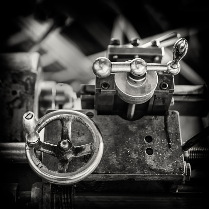 vintage image of the adjustment knobs of an antique parallel lathe for turning mechanical parts, black and white, tool carriage, square format