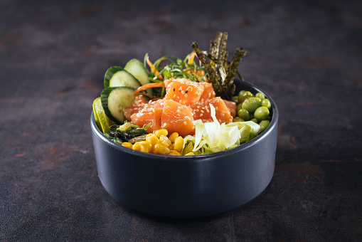 Close up shot of healthy salad bowl with sliced raw salmon ,avocado, mango and leaf vegetables above dark wooden table