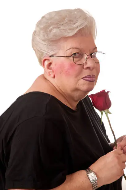 Senior woman with over done makeup looking at camera holding red rose.