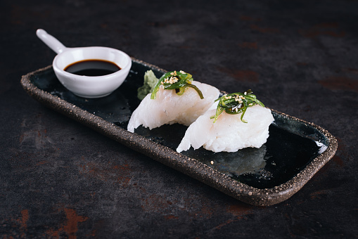 Set of sushi rolls with cream cheese, rice and salmon on a black board decorated with soy sauce and avocado on a dark wooden background. Japanese cuisine. Food photo background