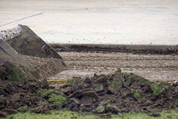 A small skid steer equipped with a bucket excavates a site which is getting an addition to the driveway.