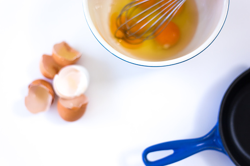 Eggs in Bowl with Whisk, Eggshells, Frying Pan, White Background