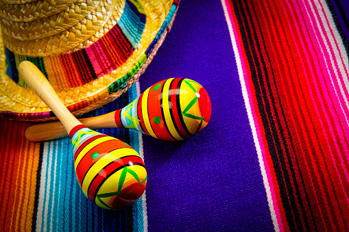 This is a photograph of a sombrero and two maracas on a colorful striped mexican blanket next to a sombrero