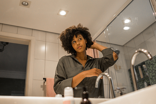 In the bathroom, a young black woman fixes her hair