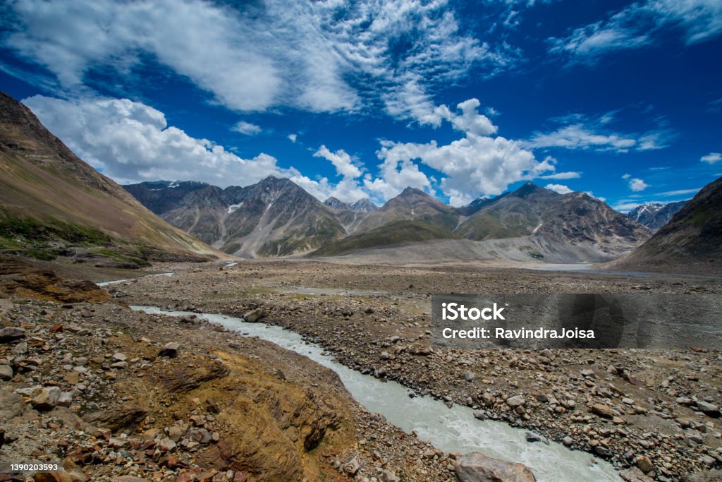 Dirt road in the mountains Dirt road in the mountains and deep below is the tributary joining the main Chenab river at Spiti valley. The landscape here is dry and looks like desert. Asia Stock Photo