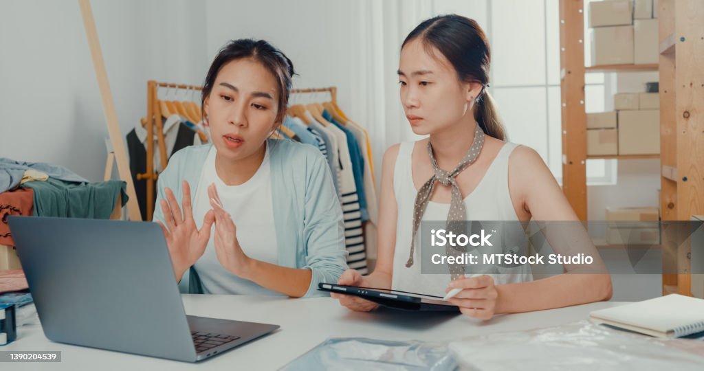 Upset young Asian women with laptop and tablet meeting check stock prepare order and plan shipping to customer at shop. Upset young women with laptop and tablet meeting check stock prepare order and plan shipping to customer at shop. Fashion Stock Photo