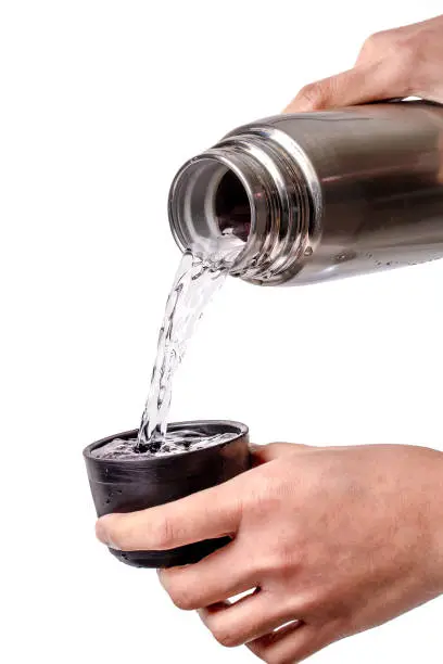 The hand was holding the stainless water bottle to pour water into the black lid isolated on a white background.