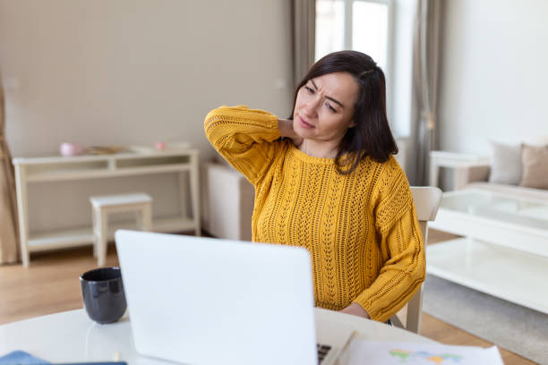 istock Feeling exhausted. Frustrated Asian woman looking exhausted and massaging her neck while sitting at her working place 1390211736