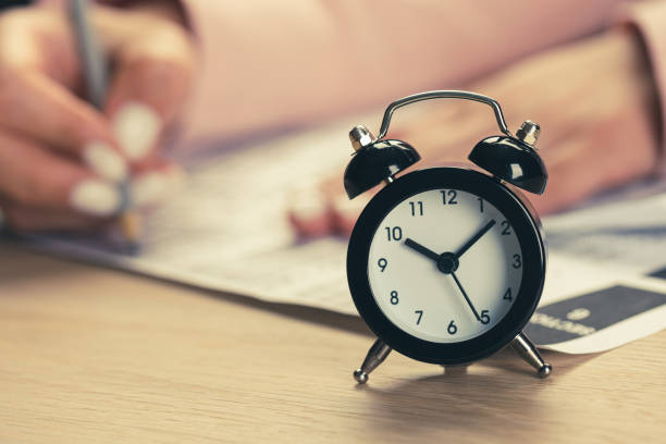istock alarm clock with time running out. Students hands to take exams, write examination room with pencil holding on optical form of standardized test with answers 1390211775