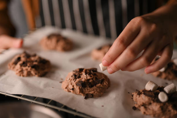 istock Female hand adding a marshmallow on a chocolate chip cookies dough 1390212952