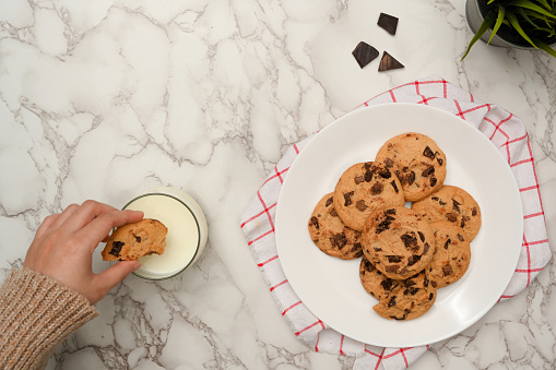 Overhead shot, A female hand dipping her cookies in a glass of milk on marble table background.