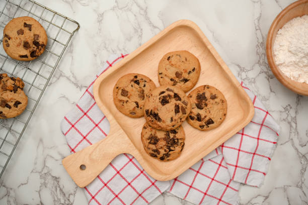 A wooden plate with chocolate cookies on marble table background Overhead image, A wooden plate with chocolate cookies on marble table background. Baked pastries. chocolate chip cookie top view stock pictures, royalty-free photos & images