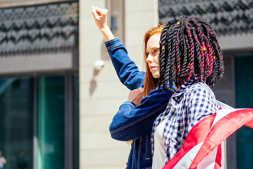lesbian redhaired ginger woman and her african american wife holding USA flag in downtown street .