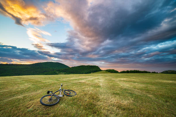Sunset dramatic sky over meadow in Marche region, Italy. MTB lying on grass amid unique hills and mountains landscape. Traveling by bicycle, alternative mobility concept.
