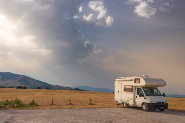 istock Camper van on road side in beautiful landscape. Dramatic sky at sunset, scenic clouds above unique highlands and hill range in Italy, alternative vanlife vacation concept. 1390217712