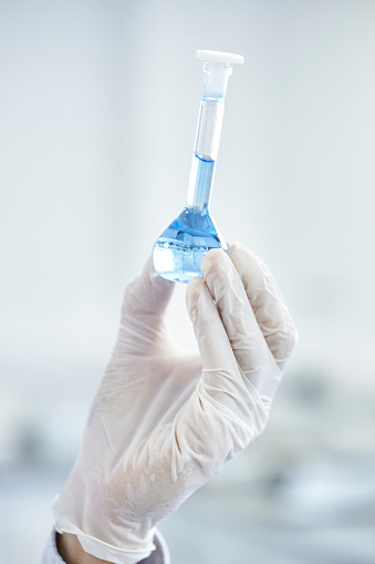 Close-up shot of a scientist's gloved hand holding a glass beaker containing a blue fluid