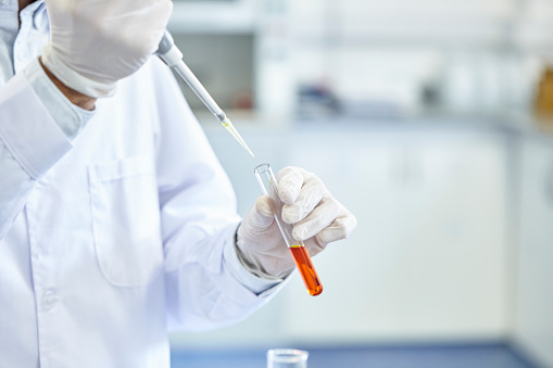 Close-up shot of a scientist's gloved hands pipetting an orange fluid into a test tube