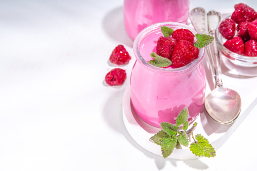 Raspberry panna cotta dessert with fresh raspberries and melissa mint leaves. Pink panna cotta in small portion jars on a white background