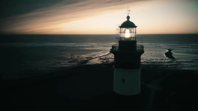 Close up of lighthouse shining head fresnel lens at dusk, drone circling around reveals sensational evening sea panorama