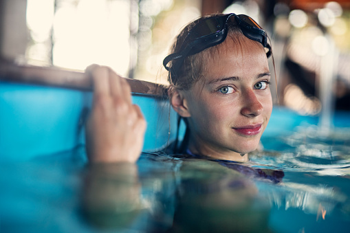 Portrait of a confident teenage girl aged 13 practicing swimming at the swimming pool. The girl is smiling at the camera.\nNikon D850