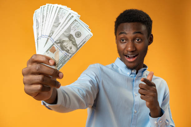 istock Excited black guy holding stack of Dollars in yellow studio 1390223263