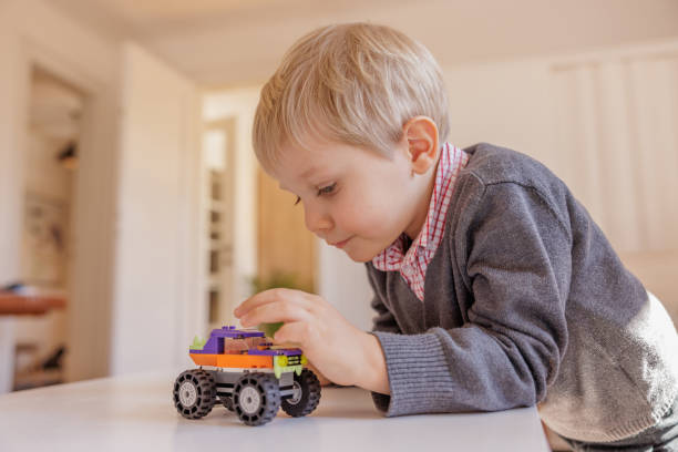 Little blond boy playing on the table at home with toy car, pushing it to move