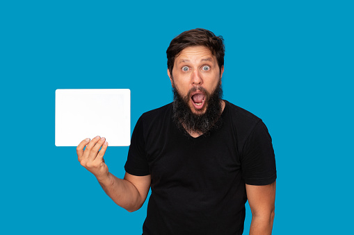 Portrait of a surprised man holding a Digital Tablet Computer blue background