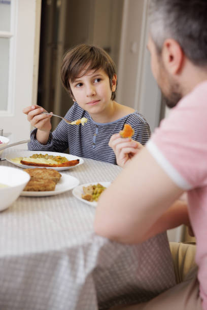 istock Boy eating with his father at the dining table at home and looking at him 1390228020