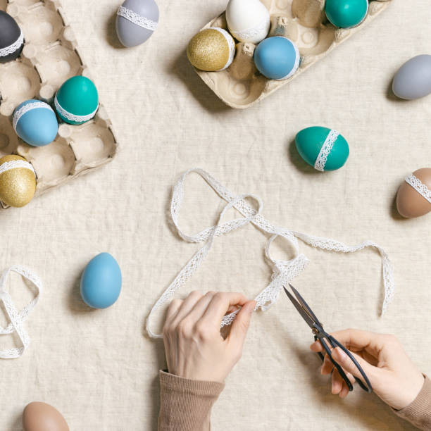 istock Decoration Easter eggs, female hands decorating colorful chicken egg with white tape lace, traditional celebration food and holiday symbol.  Home preparing for Happy Easter. Top view 1390229240