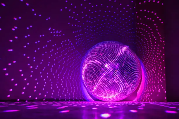 Disco ball reflecting violet light in a dark hall for discos. Holidays concept. Copy space.