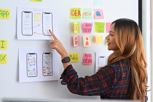Young female designer planning mobile app development prototype wireframe design on whiteboard.