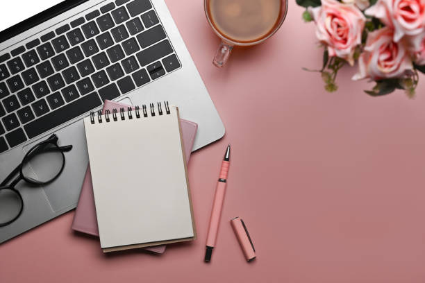 istock Laptop computer, coffee cup, blank notepad and flowers on pink background. Flat lay, Top view, Copy space. 1390233731