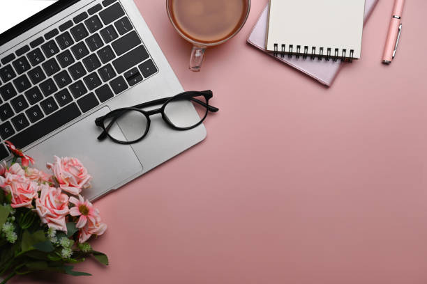 istock Home office desk with blank notebook, laptop computer and pink roses bouquet on pink background. Flat lay. 1390233758
