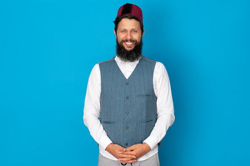 Ottoman man with long beard on blue background wearing fez, shirt and bolero
