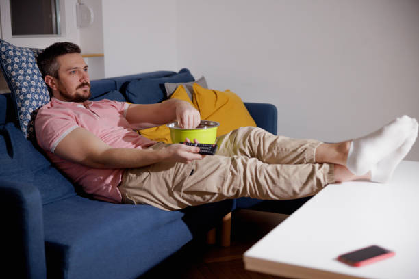 istock Man leaning on the sofa with feet up on coffee table and changing channels 1390237950