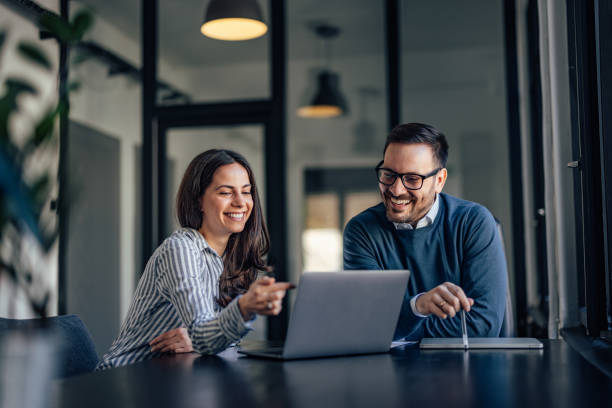Smiling people, in the meeting room, using a laptop, searching s Smiling brunette girl, showing something online to her boss. professional woman smiling stock pictures, royalty-free photos & images