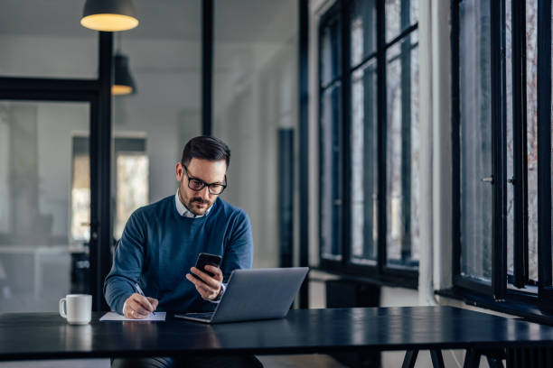 istock Focused man, reading something from his phone, writing on a paper. 1390244810