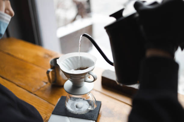 donna barista che versa acqua calda sul caffè marrone macinato attraverso il filtro antigoccia. - brown candid caffein drink foto e immagini stock