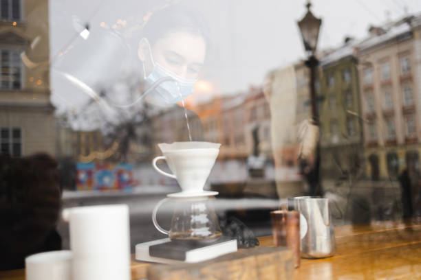 la ragazza prepara il caffè attraverso un filtro in un metodo a goccia e lo versa in una tazza di vetro - brown candid caffein drink foto e immagini stock