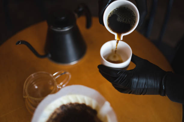 la ragazza prepara il caffè attraverso un filtro in un metodo a goccia e lo versa in una tazza di vetro - brown candid caffein drink foto e immagini stock