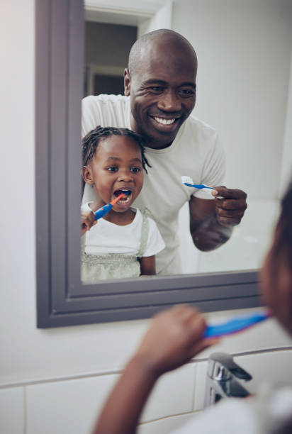 aufnahme eines kleinen mädchens und ihres vaters, die sich zu hause die zähne putzen - little girls african descent black small stock-fotos und bilder