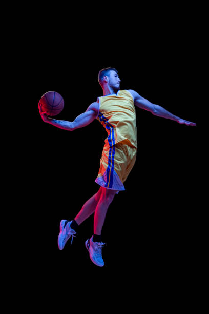Portrait of sportive man, professional basketball player playing basketball isolated on dark background in neon light. Achievements, sport career, motion concepts. Slam dunk. Portrait of sportive professional basketball player jumping high with ball isolated on dark background in neon light. Concept of sport, achievements, competition, hobby, active lifestyle. silhouette of basketball player slam dunk stock pictures, royalty-free photos & images