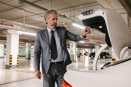 A senior businessman closes a trunk in a parking lot